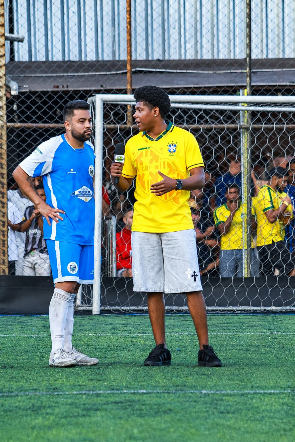 Teodoro com o microfone durante uma entrevista com um jogador de uniforme azul e branco.