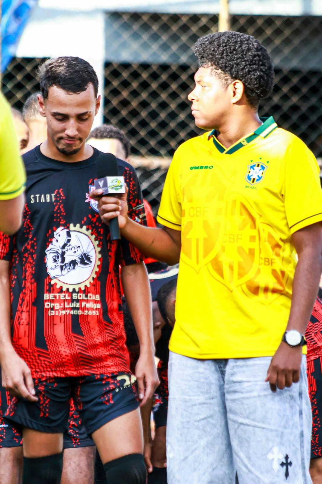 Teodoro e um jogador de uniforme vermelho e preto durante uma entrevista.