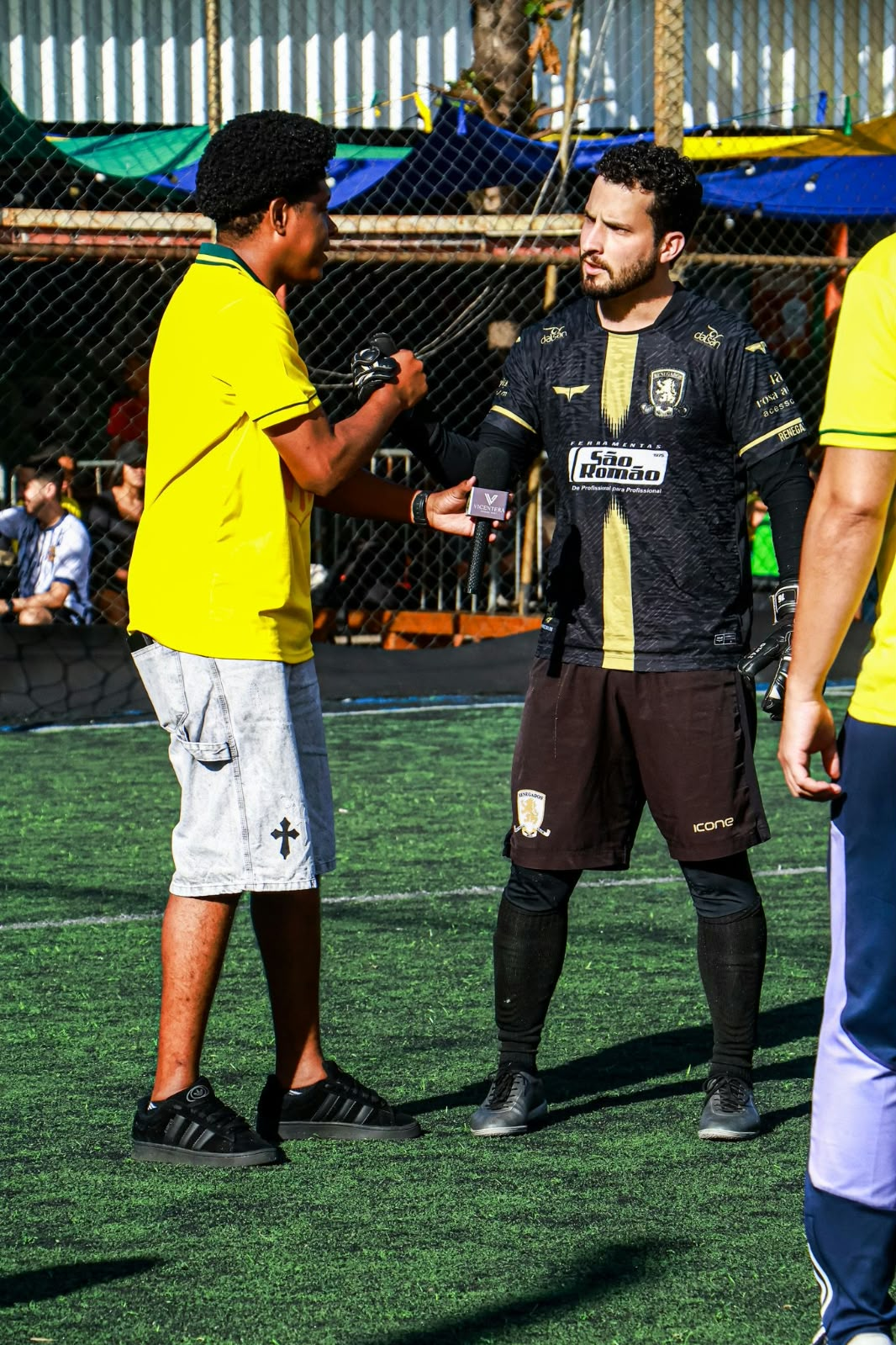 Teodoro entrevistando um jogador de uniforme preto com um microfone.